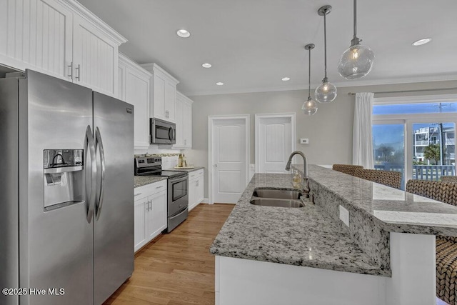 kitchen featuring a kitchen island with sink, a sink, white cabinetry, appliances with stainless steel finishes, and pendant lighting