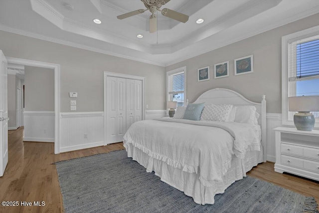 bedroom featuring a wainscoted wall, a closet, a raised ceiling, and wood finished floors