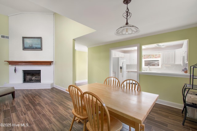 dining room with a fireplace, visible vents, baseboards, dark wood-style floors, and crown molding