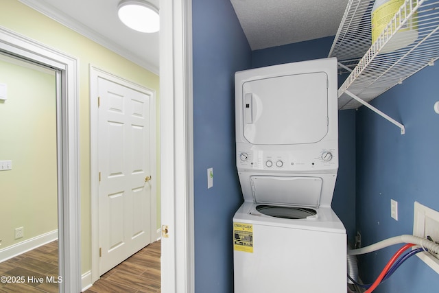 laundry area with laundry area, wood finished floors, stacked washer and clothes dryer, and baseboards