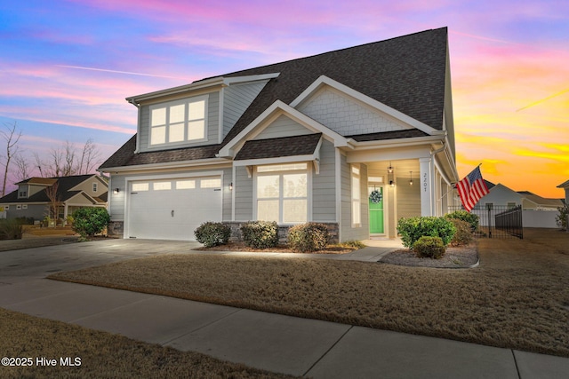 craftsman-style house with a shingled roof, concrete driveway, an attached garage, fence, and stone siding