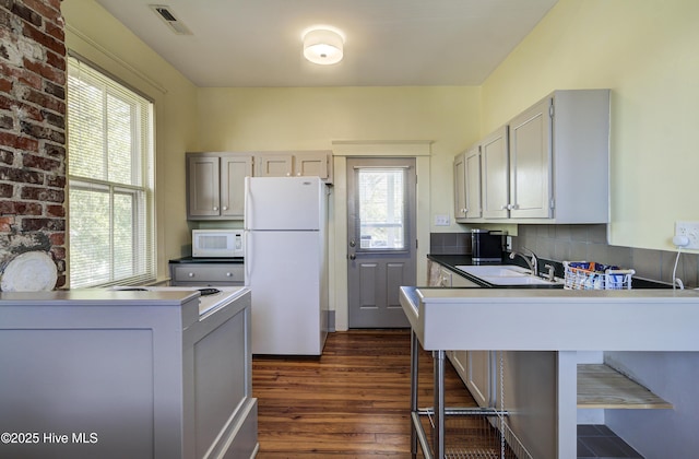 kitchen with sink, white appliances, dark hardwood / wood-style floors, tasteful backsplash, and a kitchen bar