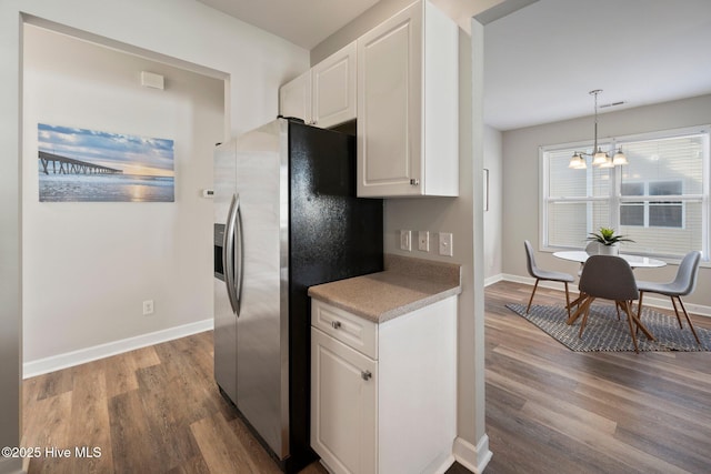 kitchen featuring white cabinetry, hardwood / wood-style floors, stainless steel fridge, and decorative light fixtures