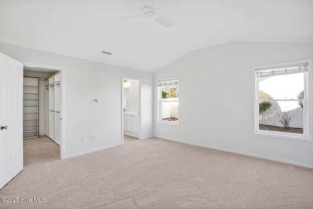 unfurnished bedroom with light colored carpet, a walk in closet, ensuite bath, vaulted ceiling, and ceiling fan