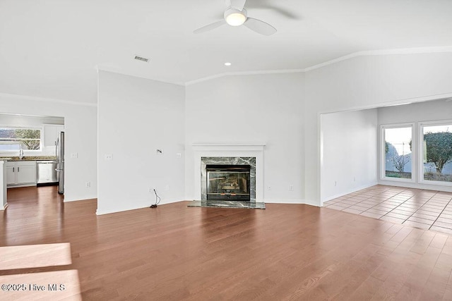 unfurnished living room featuring ornamental molding, hardwood / wood-style flooring, a high end fireplace, and ceiling fan