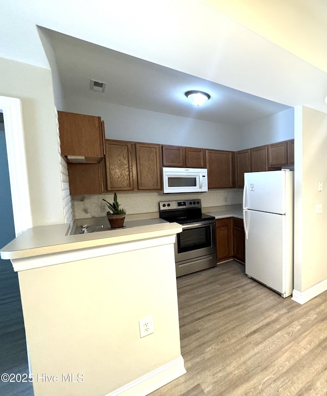 kitchen featuring tasteful backsplash, light hardwood / wood-style flooring, white appliances, and kitchen peninsula