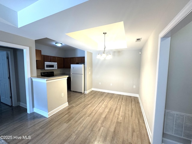 kitchen with pendant lighting, white appliances, a notable chandelier, light hardwood / wood-style floors, and a raised ceiling