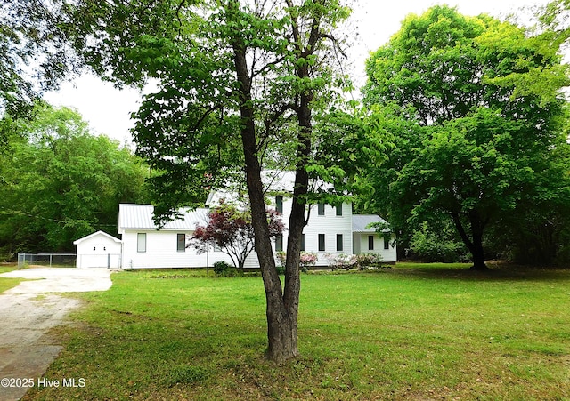 view of front of property featuring an outbuilding, concrete driveway, a front lawn, and metal roof