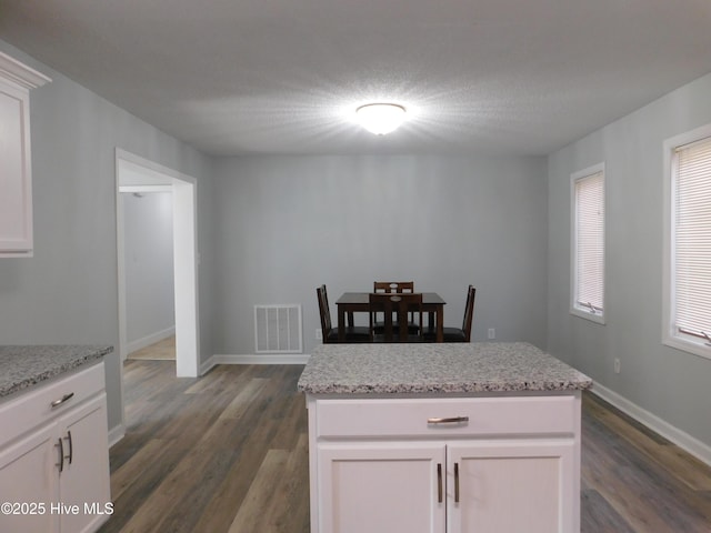 kitchen with light stone counters, a kitchen island, and white cabinets