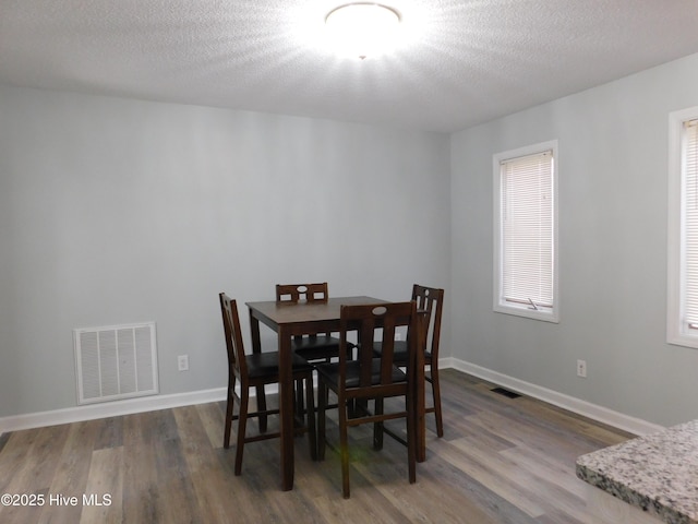 dining area with visible vents, baseboards, wood finished floors, and a textured ceiling