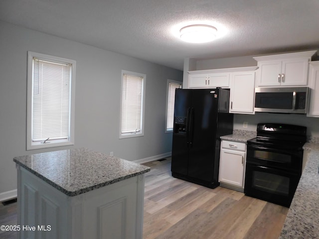 kitchen with white cabinets, light stone countertops, light wood-type flooring, and black appliances