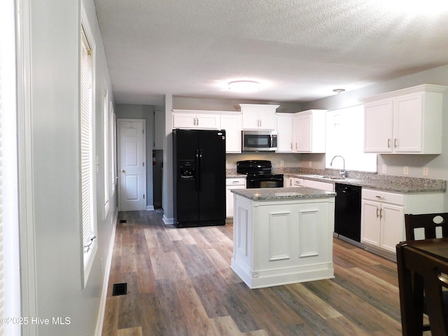 kitchen with light stone counters, black appliances, a center island, hardwood / wood-style flooring, and white cabinets