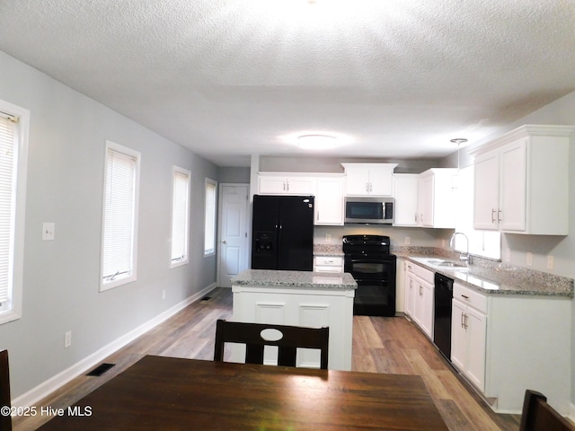 kitchen featuring visible vents, a sink, light wood-type flooring, white cabinetry, and black appliances