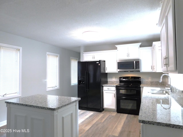kitchen with black appliances, light stone countertops, a healthy amount of sunlight, light wood finished floors, and a sink