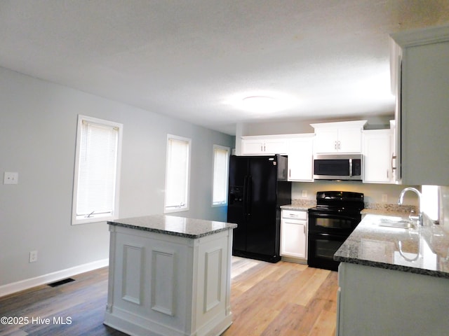 kitchen featuring visible vents, a sink, black appliances, and dark stone counters