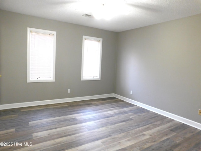 unfurnished room with dark wood-type flooring, visible vents, and baseboards
