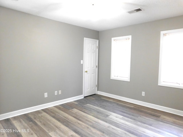 unfurnished room with a healthy amount of sunlight, wood finished floors, baseboards, and visible vents
