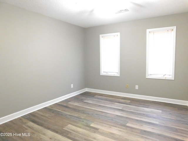 empty room featuring dark wood-style flooring, baseboards, and visible vents