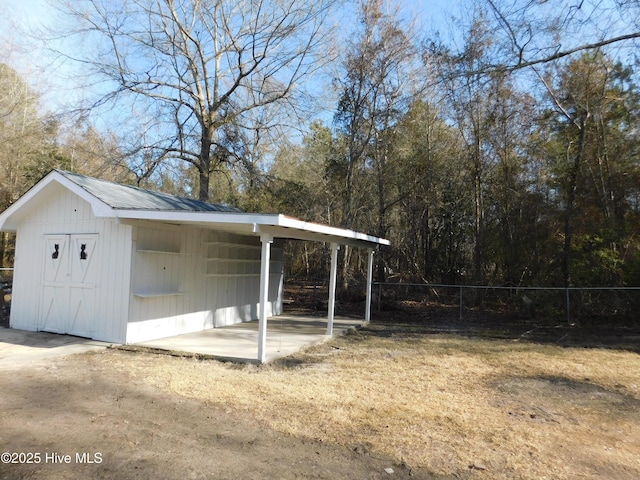 view of outdoor structure with a carport, fence, and an outbuilding