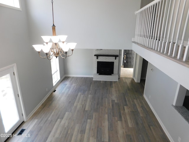 unfurnished living room with a chandelier, a fireplace, dark hardwood / wood-style flooring, and a high ceiling