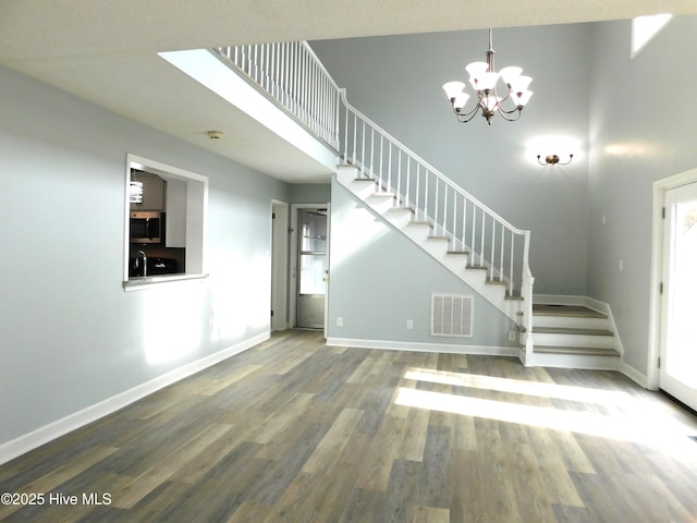 unfurnished living room with visible vents, baseboards, a notable chandelier, stairway, and wood finished floors