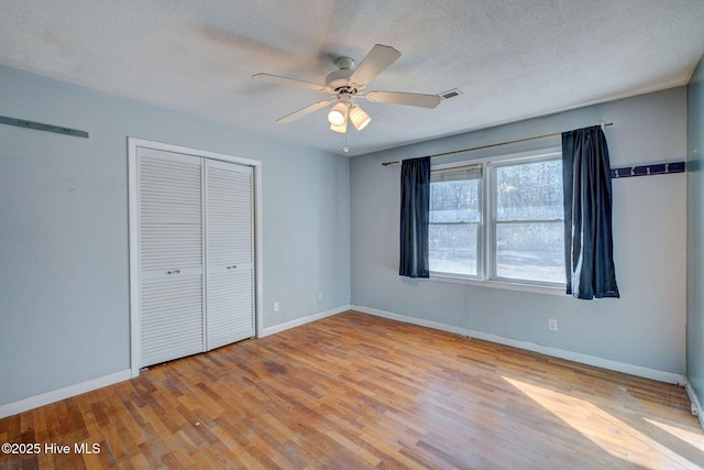 unfurnished bedroom featuring ceiling fan, a closet, a textured ceiling, and light wood-type flooring