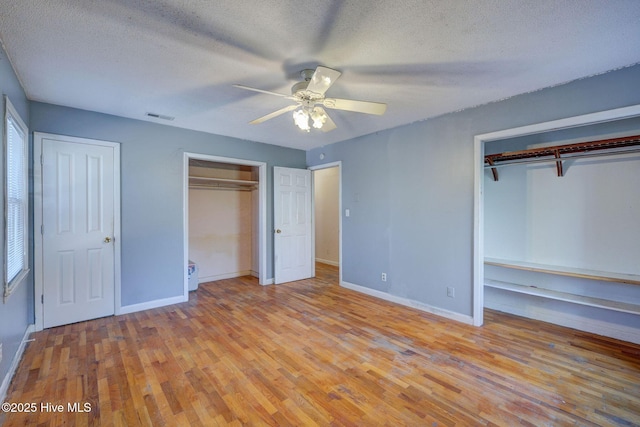 unfurnished bedroom with a textured ceiling, two closets, ceiling fan, light hardwood / wood-style floors, and multiple windows