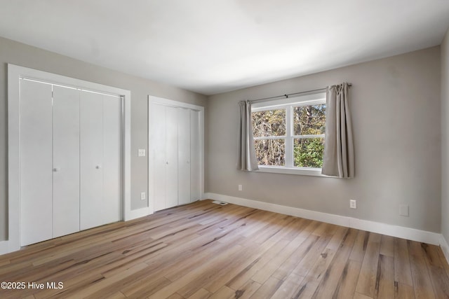 unfurnished bedroom featuring light hardwood / wood-style floors and two closets