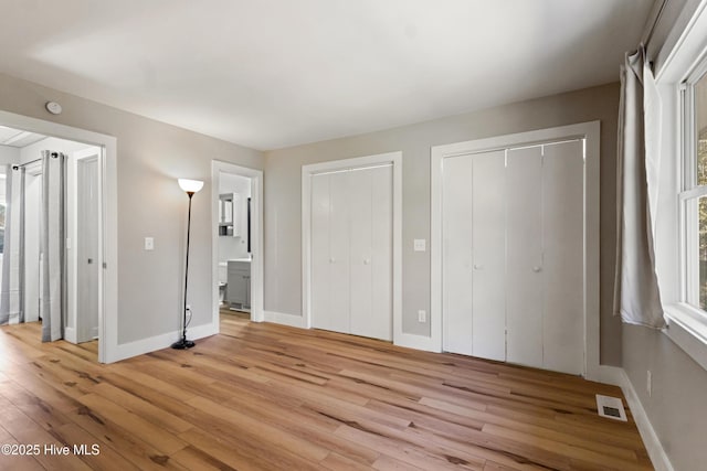 unfurnished bedroom featuring multiple closets, ensuite bathroom, and light hardwood / wood-style floors