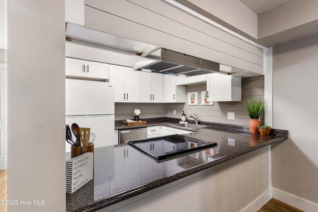 kitchen with sink, white cabinetry, island range hood, dark stone countertops, and white fridge