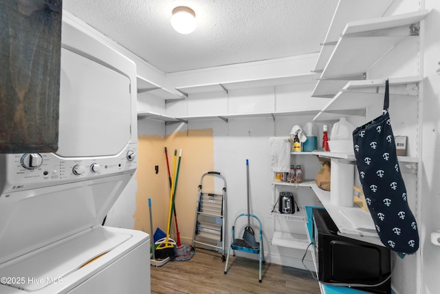 clothes washing area with laundry area, a textured ceiling, stacked washing maching and dryer, and wood finished floors