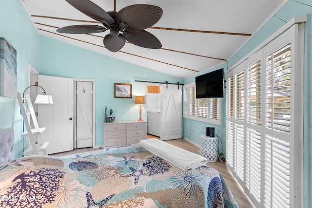 bedroom with light wood-style flooring, vaulted ceiling, a ceiling fan, and a barn door