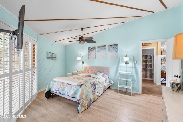 bedroom featuring vaulted ceiling, light hardwood / wood-style floors, ceiling fan, and wood walls