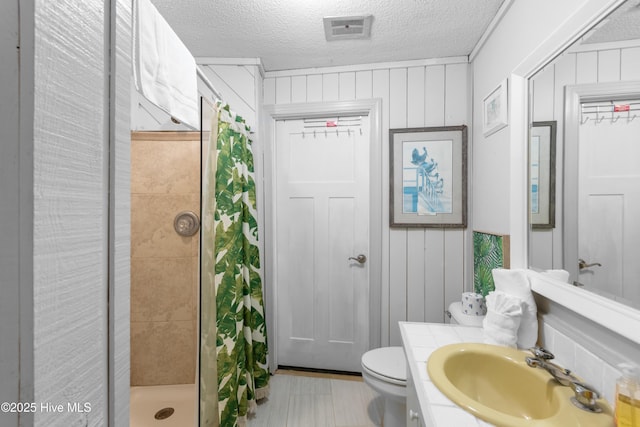 bathroom with a textured ceiling, toilet, vanity, visible vents, and a shower stall