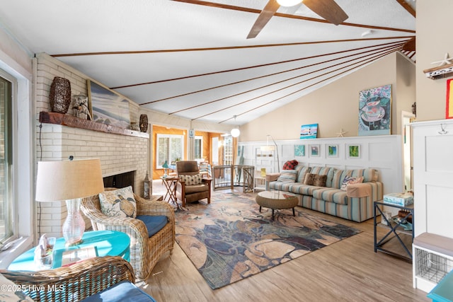 living room featuring ceiling fan, lofted ceiling, a brick fireplace, and wood-type flooring