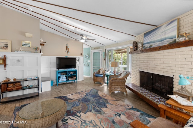 living room with a brick fireplace, hardwood / wood-style flooring, vaulted ceiling, and ceiling fan