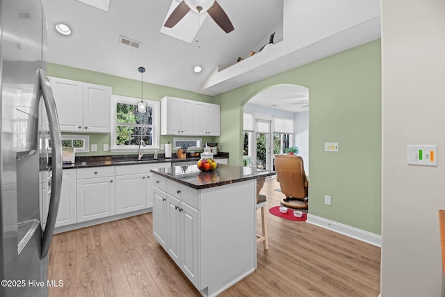 kitchen featuring pendant lighting, stainless steel refrigerator, white cabinetry, a kitchen breakfast bar, and a center island