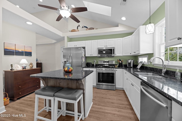 kitchen featuring sink, a breakfast bar area, dark stone countertops, stainless steel appliances, and white cabinets