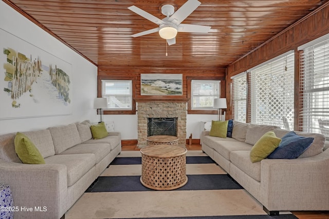 living room with wood ceiling, ceiling fan, a stone fireplace, and a wealth of natural light