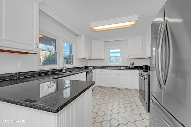 kitchen featuring sink, crown molding, dark stone countertops, stainless steel appliances, and white cabinets