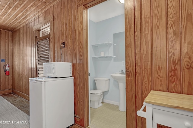 bathroom featuring toilet, sink, wooden walls, and washer / clothes dryer