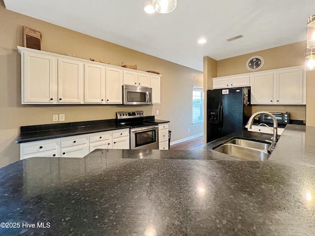 kitchen with appliances with stainless steel finishes, sink, white cabinets, dark stone counters, and hanging light fixtures