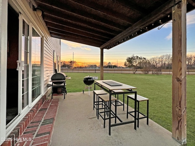 patio terrace at dusk featuring area for grilling and a lawn