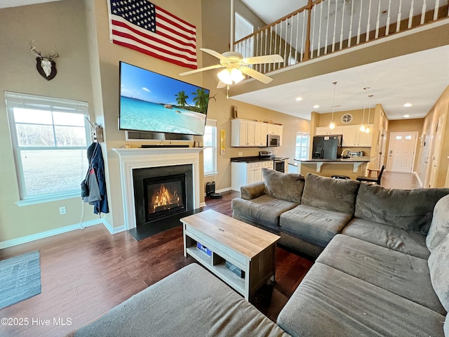 living room featuring a wealth of natural light, dark wood-type flooring, ceiling fan, and a high ceiling