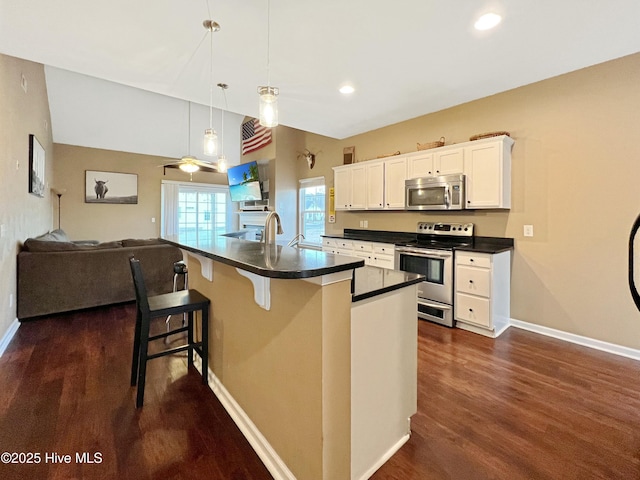 kitchen featuring appliances with stainless steel finishes, white cabinetry, a breakfast bar area, hanging light fixtures, and dark wood-type flooring