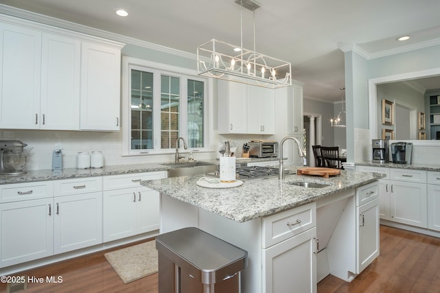 kitchen featuring pendant lighting, white cabinetry, a notable chandelier, ornamental molding, and an island with sink