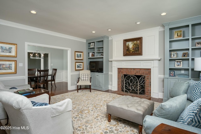 living room with built in features, ornamental molding, dark hardwood / wood-style flooring, a brick fireplace, and a chandelier