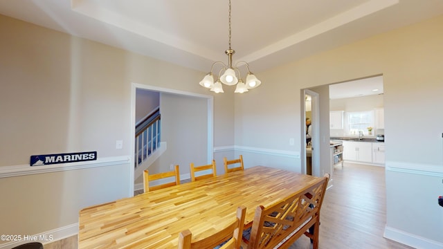 dining area with light wood-type flooring, an inviting chandelier, stairs, and a raised ceiling
