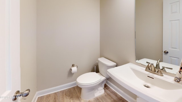 bathroom featuring baseboards, wood finished floors, a sink, and toilet