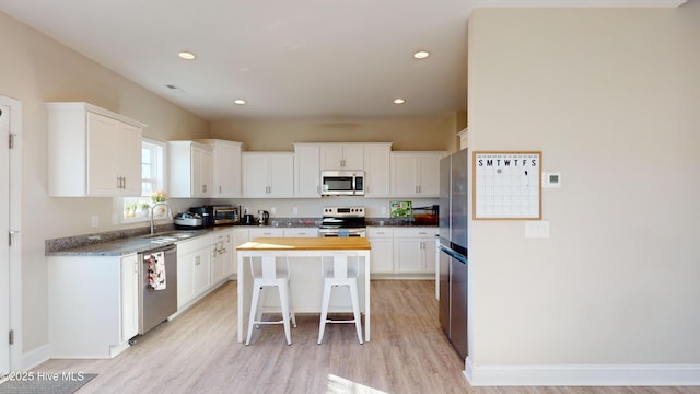 kitchen featuring appliances with stainless steel finishes, white cabinetry, sink, a breakfast bar area, and a center island